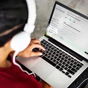User is scrolling LMS on the Macbook with headphones on.